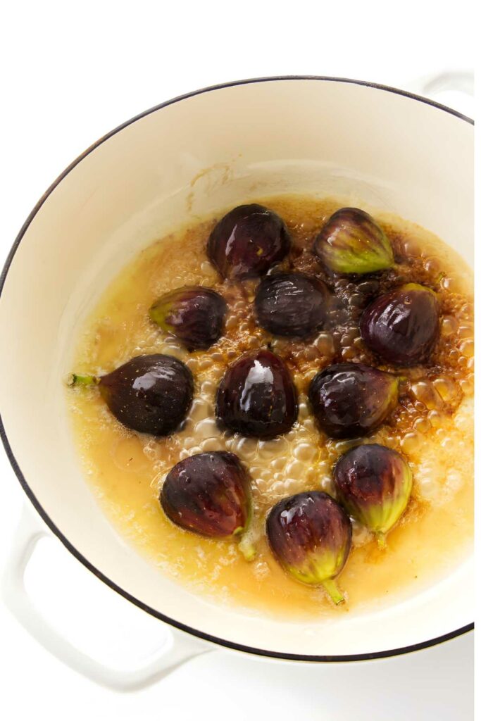Whole figs simmer in brown liquid inside a white pot.