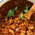 Charro beans with bacon and cilantro in a pot, wooden spoon stirring.