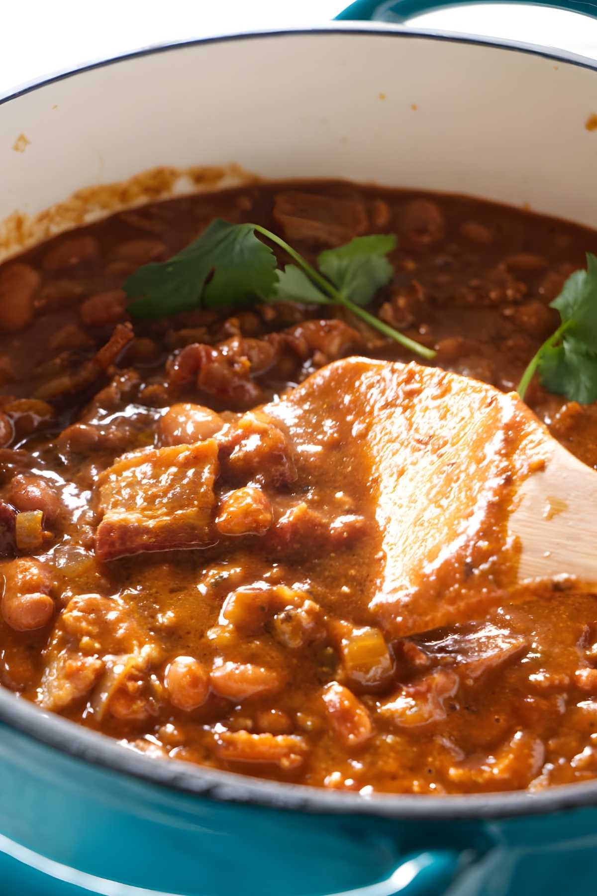 A spoon in a pot of charro beans with bacon.
