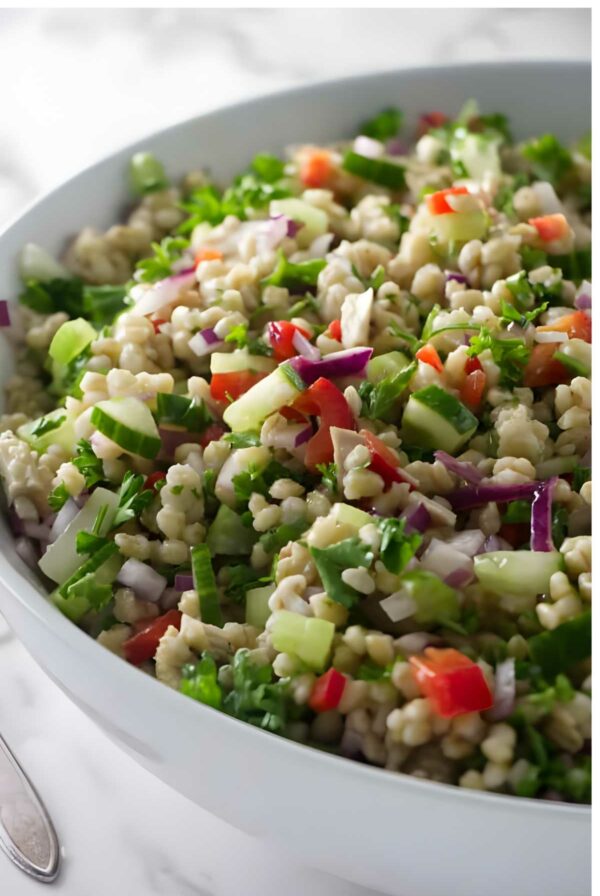 Close-up of barley salad with veggies in a white bowl on marble surface.