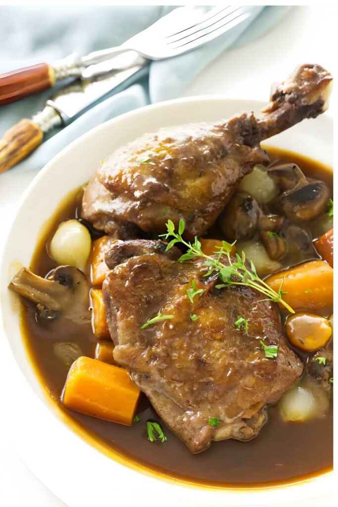 Coq au vin with chicken, vegetables, and sauce, garnished with thyme on plate.