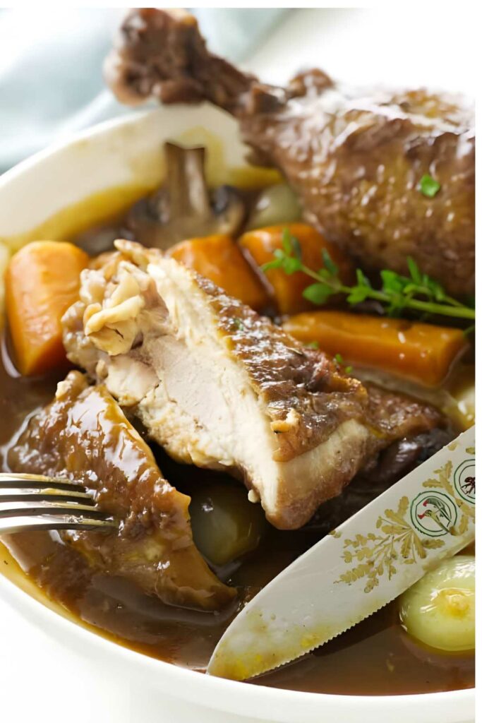 Red wine chicken with carrots, onions, and mushrooms in sauce, herbs on top.