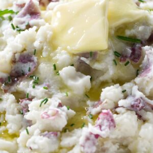 Chunky mashed potatoes with red peels, butter, and chives in a bowl.
