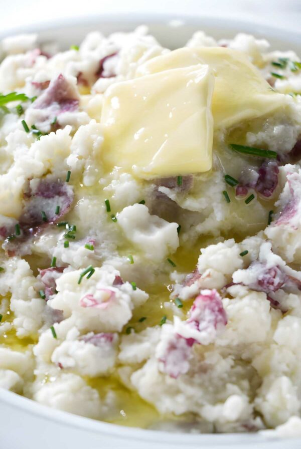 Chunky mashed potatoes with red peels, butter, and chives in a bowl.