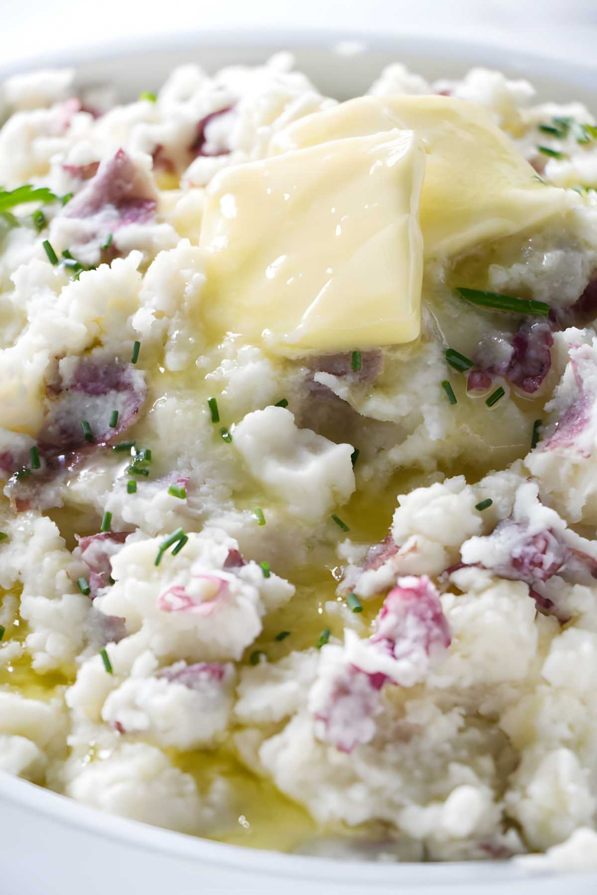 Chunky mashed potatoes with red peels, butter, and chives in a bowl.