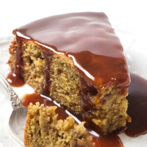Moist cake slice with caramel sauce on white plate, forkful in front.
