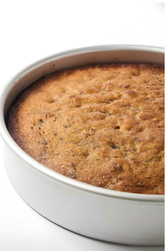 Golden-brown date cake in a white pan on a white background, looks moist.