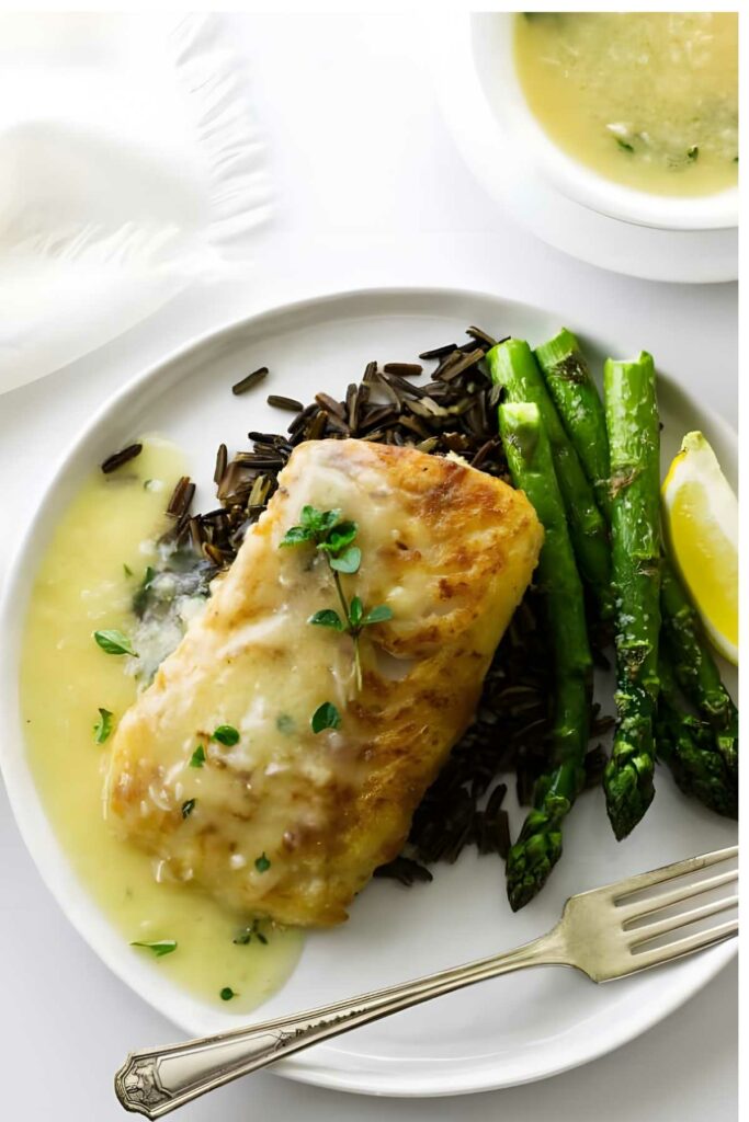 Pan seared cod with creamy sauce on wild rice and asparagus, lemon wedge, fork.