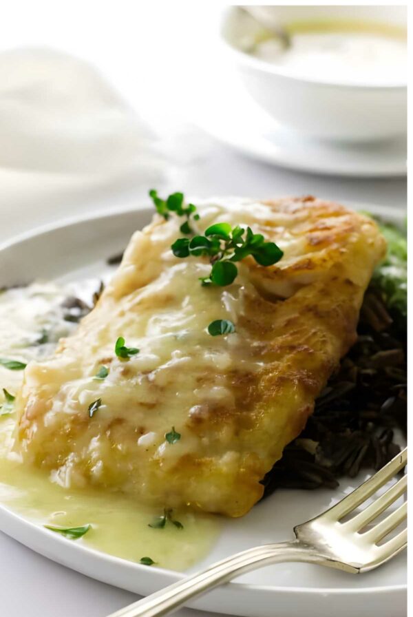 Seared cod fish fillet with creamy sauce and herbs on wild rice.