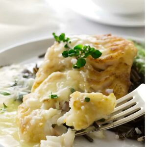 Fork holds baked white fish with lemon sauce, wild rice, and greens.