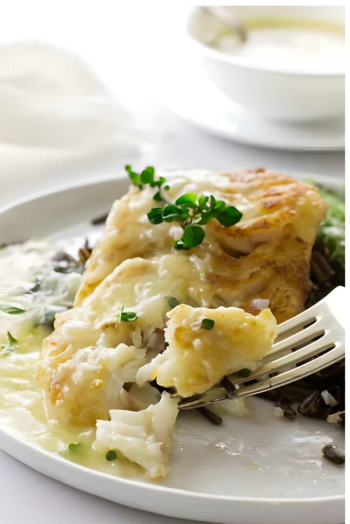 Fork holds seared cod fish with lemon sauce, wild rice, and greens.
