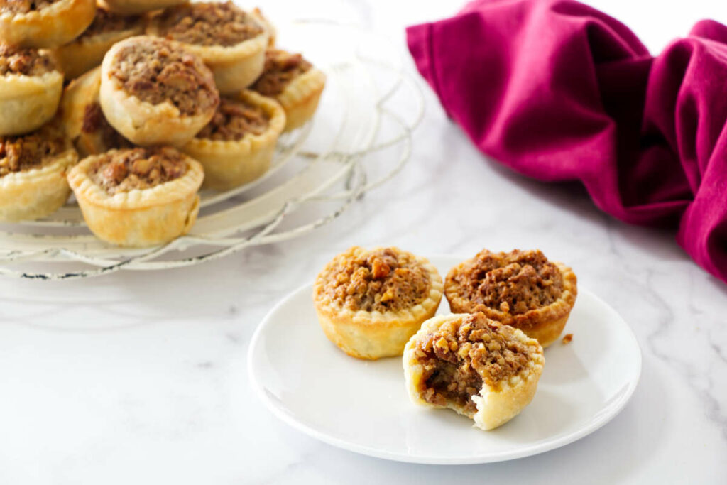 Three pecan pie cookies on a plate with more tassies in the back.
