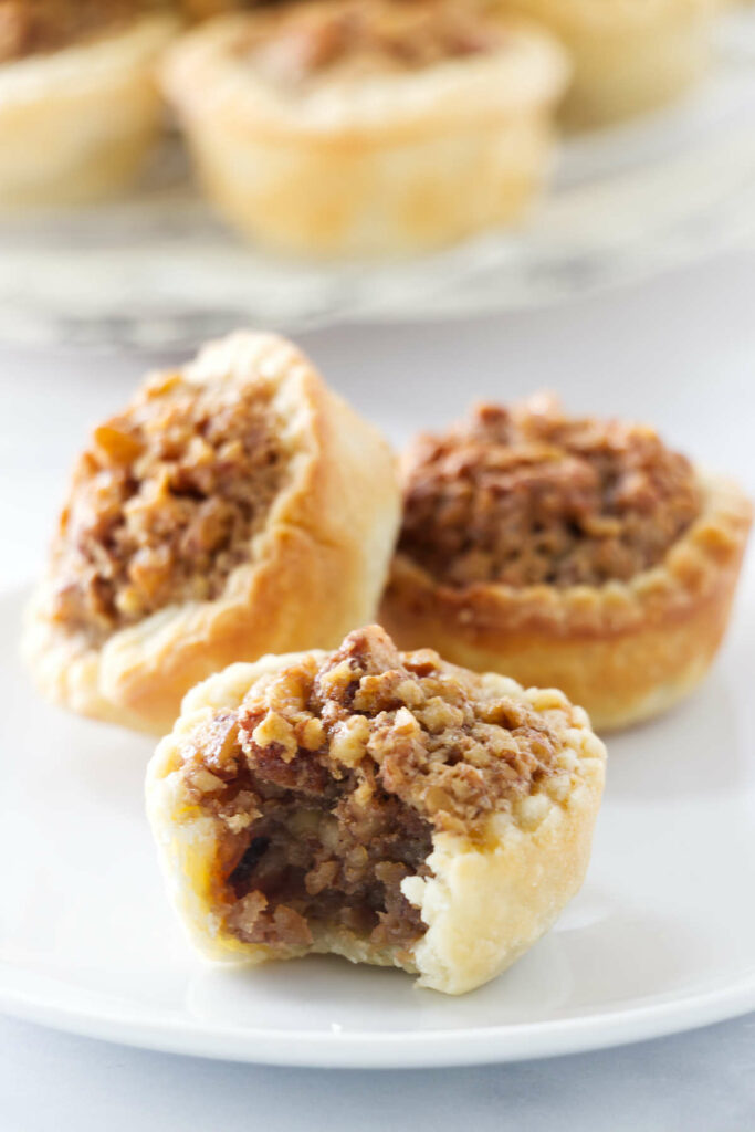 Three pecan tassies on a white plate, one partially eaten.