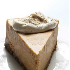 Pumpkin cheesecake slice with whipped cream on a white plate.