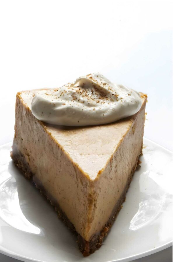 Pumpkin cheesecake slice with whipped cream on a white plate.