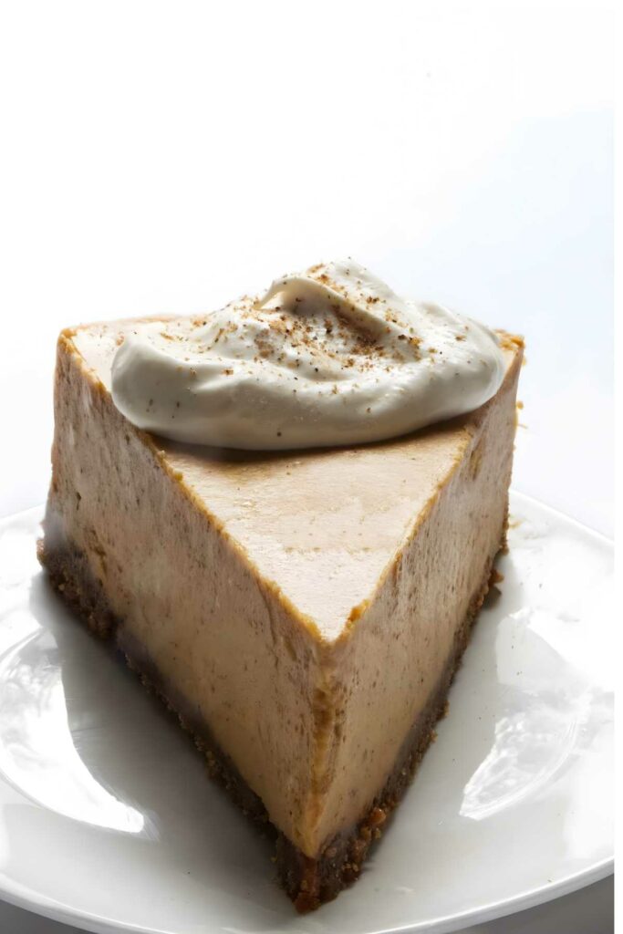 Pumpkin cheesecake slice with whipped cream on a white plate.