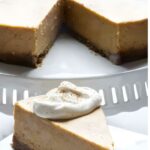 Cheesecake slice with whipped cream on plate, whole cake behind, wedge missing.