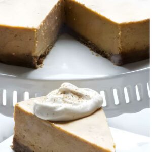 Cheesecake slice with whipped cream on plate, whole cake behind, wedge missing.