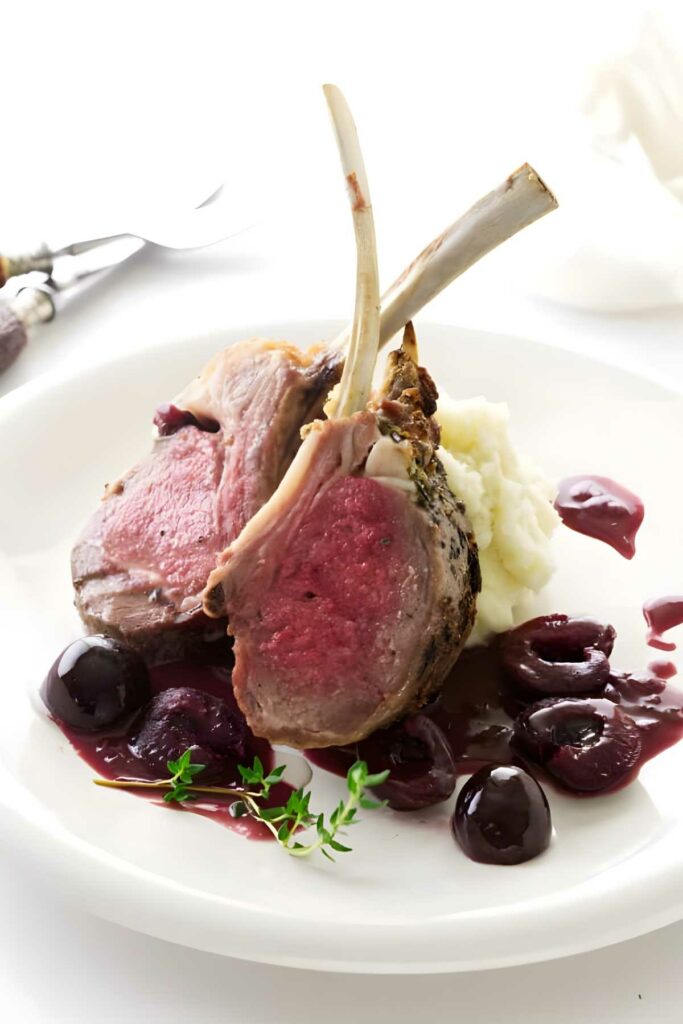Rack of lamb with mashed potatoes, cherry sauce, and thyme on white plate.