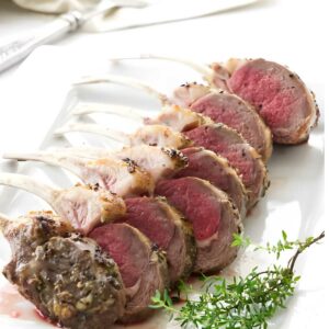 Sliced medium-rare rack of lamb on white plate with thyme garnish.