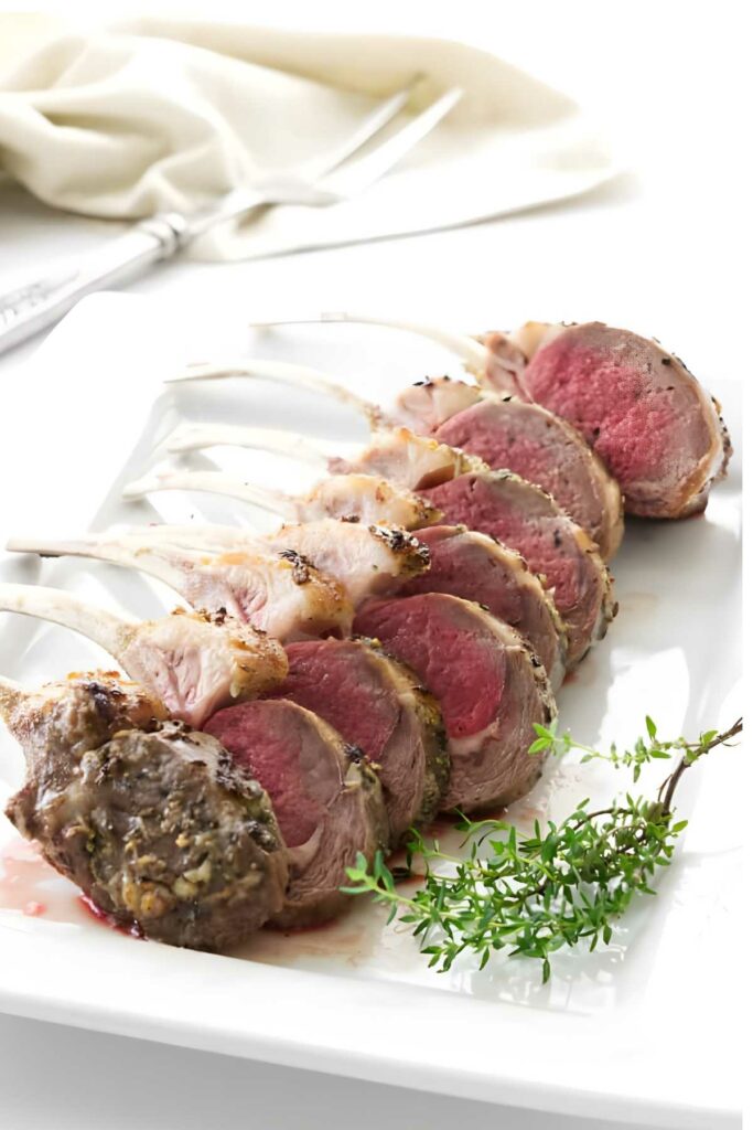 Sliced medium-rare rack of lamb on white plate with thyme garnish.