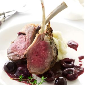 Cherry glazed rack of lamb with mashed potatoes, cherry sauce, and thyme on white plate.