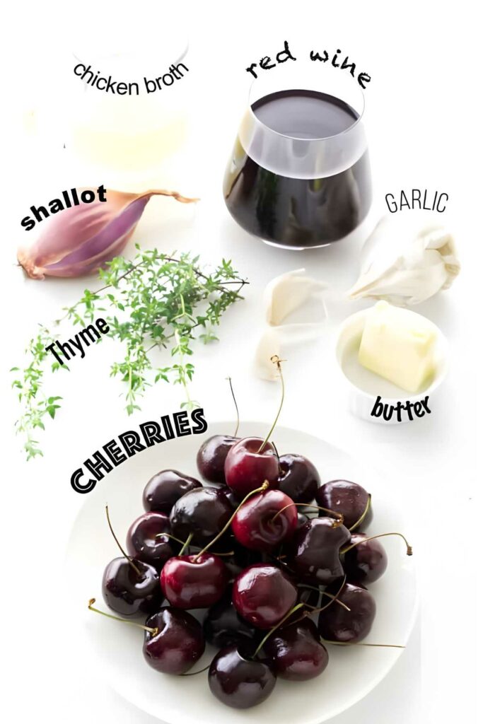 Recipe ingredients on white surface: cherries, thyme, shallot, garlic, butter, wine, broth.