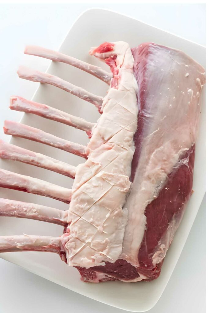 Raw rack of lamb with scored fat on a white plate.
