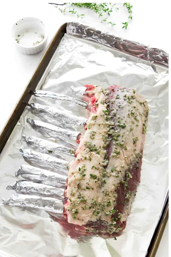 Herb and garlic rack of lamb on foil-lined sheet, rib bones wrapped in foil.