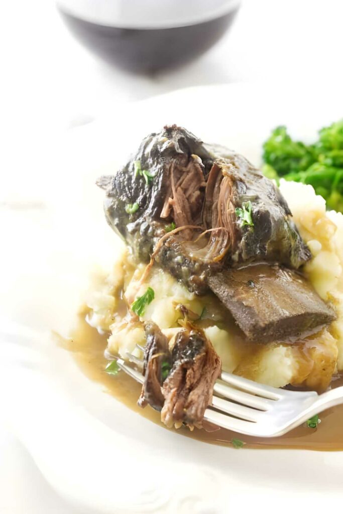 Mashed potatoes with garlic braised short ribs and green vegetables on a plate.
