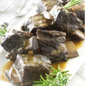 Braised beef short ribs with brown gravy and rosemary on a white plate.
