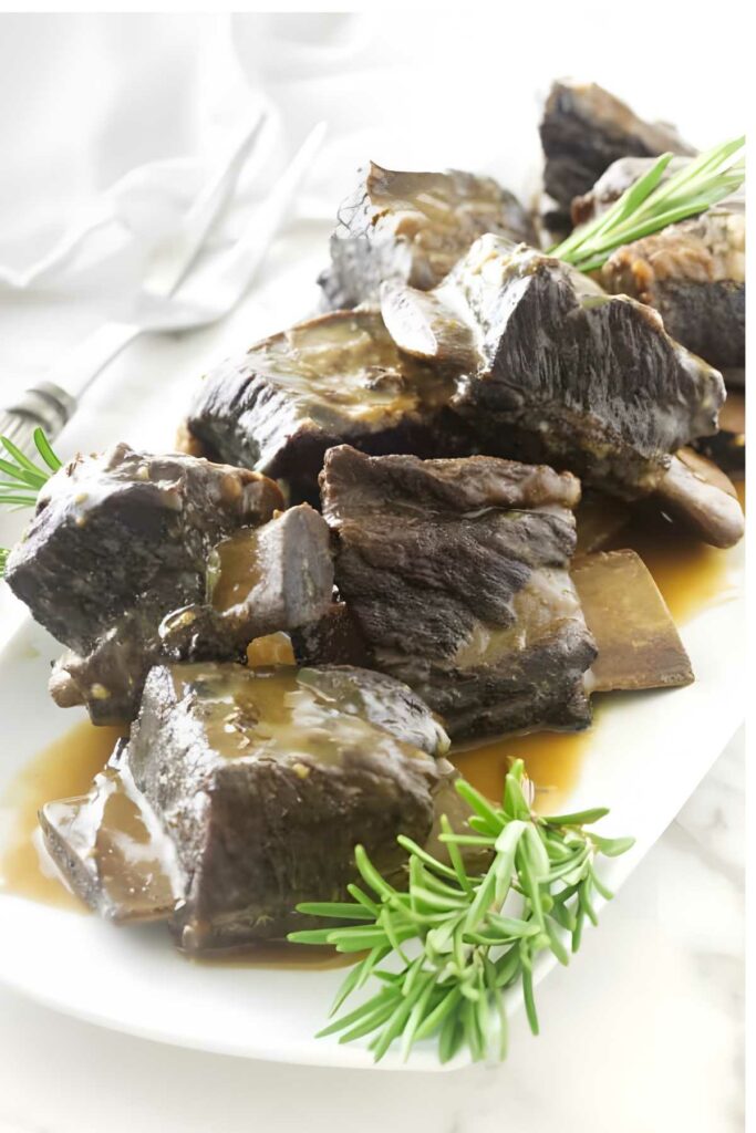 Braised beef short ribs with brown gravy and rosemary on a white plate.