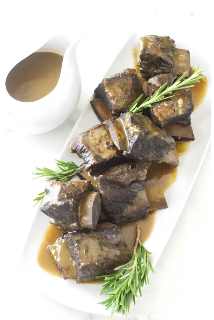 Braised short ribs with brown gravy, rosemary garnish, and a gravy boat.