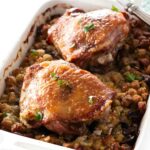 Roasted turkey thighs on stuffing in a white dish, garnished with herbs.