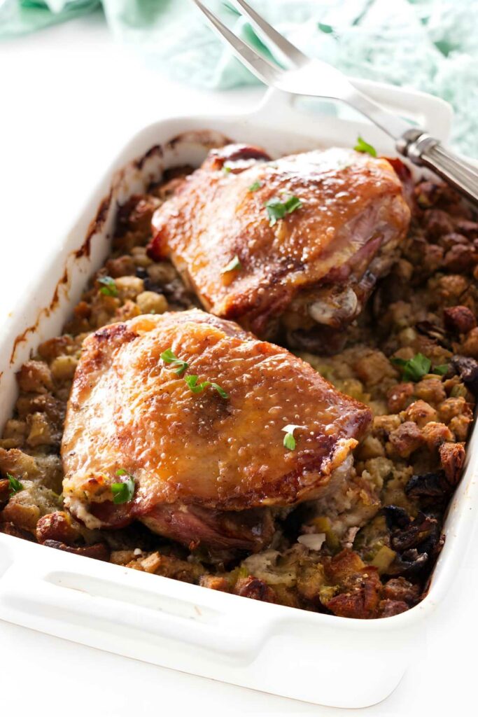 Roasted turkey thighs on stuffing in a white dish, garnished with herbs.