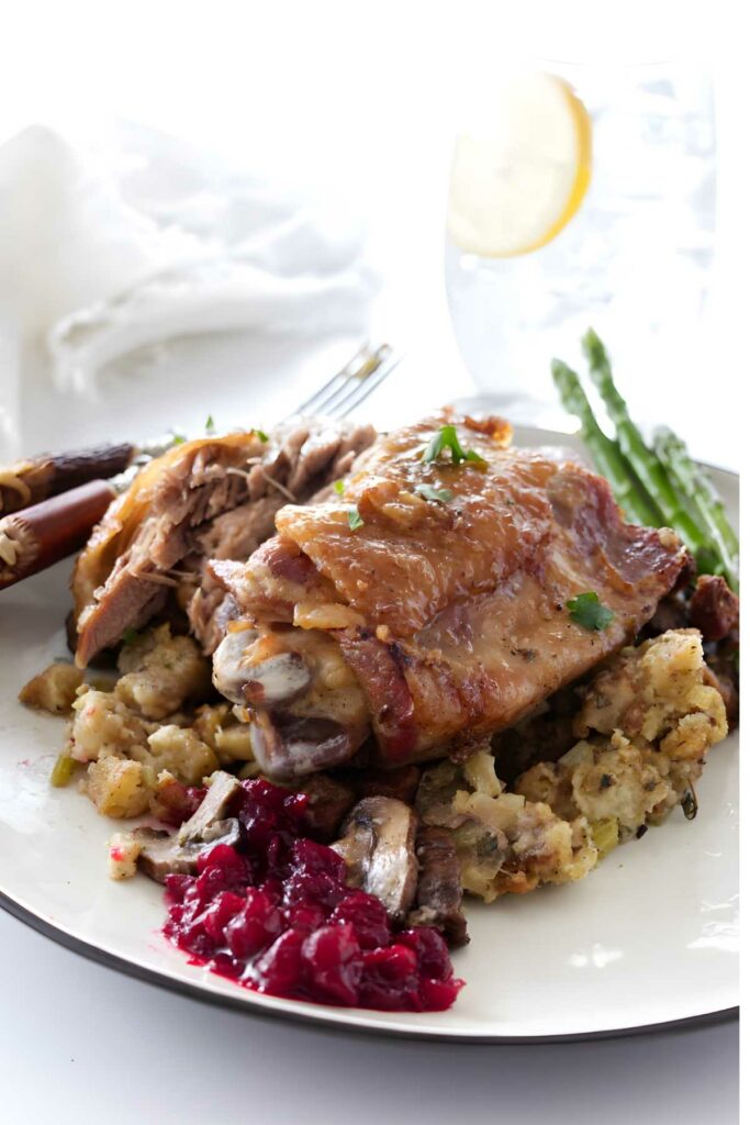 Roast turkey thigh on stuffing with asparagus and cranberry sauce, water glass behind.