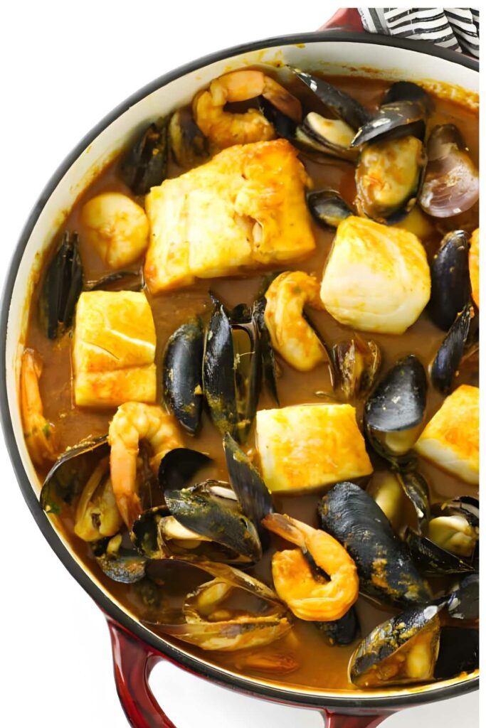 Seafood stew with shrimp and mussels in a red-handled pot, top view.