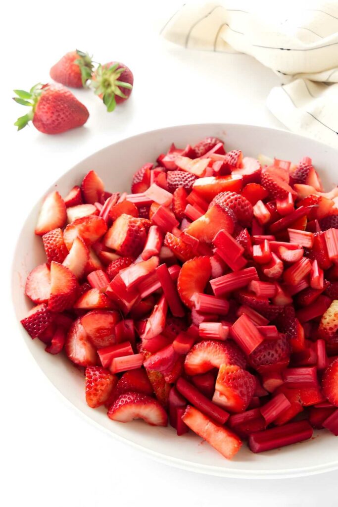 Bowl of chopped strawberries and rhubarb on a white surface.