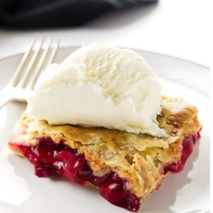 Slice of strawberry rhubarb pie with ice cream on a white plate.