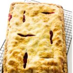 Rectangular fruit pie with golden crust and red filling cooling on wire rack.
