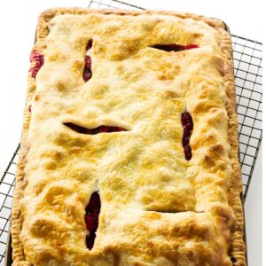Rectangular fruit pie with golden crust and red filling cooling on wire rack.