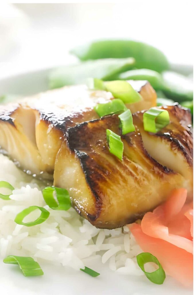 Seared glazed fish on rice with green onions, ginger, and vegetables.