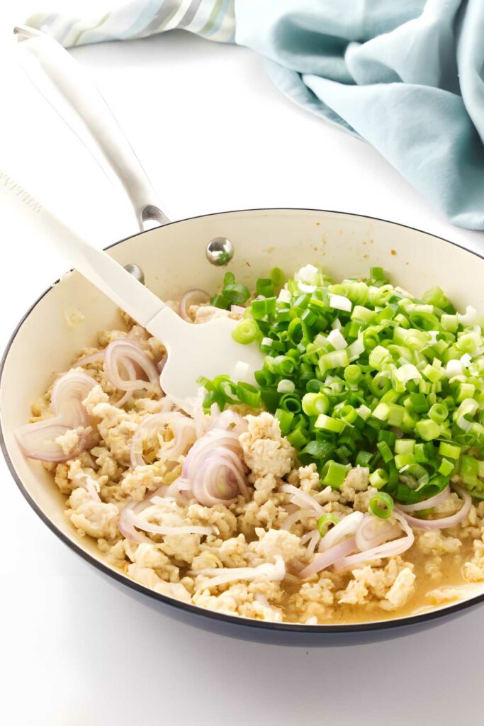 Ground chicken, shallots, and green onions being stirred in a skillet.