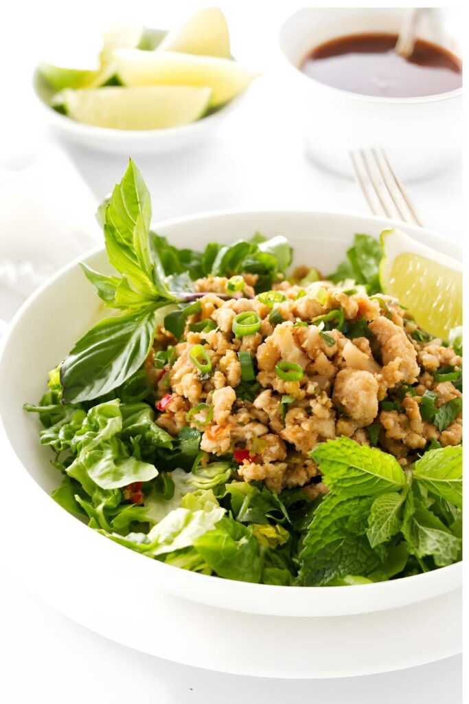 Minced chicken salad with herbs in a white bowl, lime garnish.