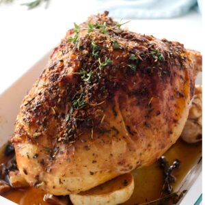 Herb-crusted roasted turkey breast in a white dish with thyme and rosemary.