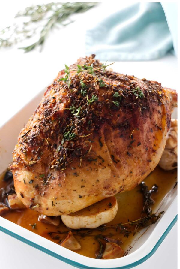 Herb-crusted roasted turkey breast in a white dish with thyme and rosemary.