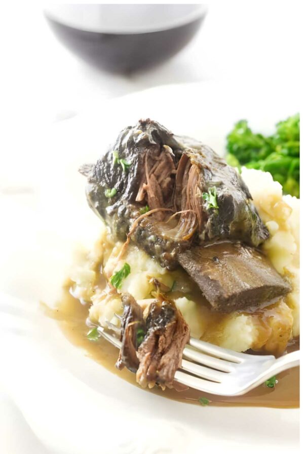 Braised short ribs on mashed potatoes with gravy and herbs, broccoli in background.