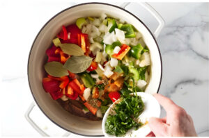 Adding bay leaves and seasonings to a pot for making gumbo.