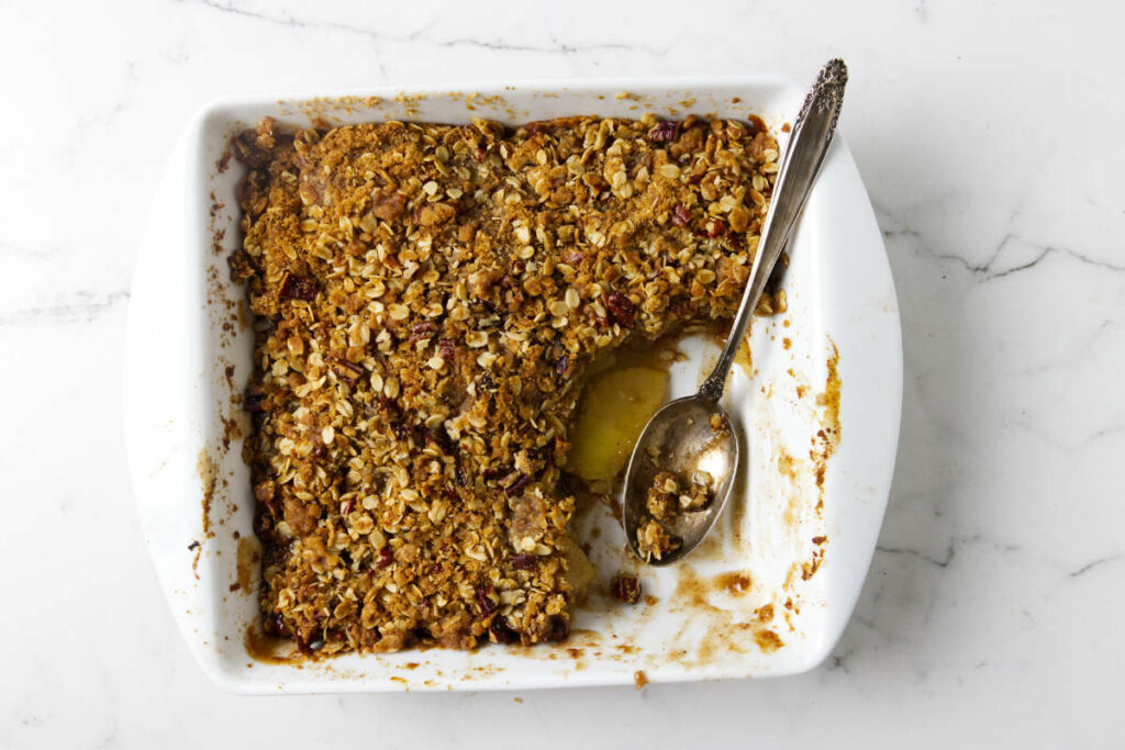 A spoon in a baking dish with apple crisp.