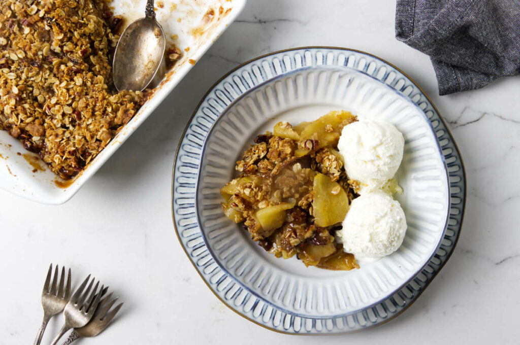 A serving of homemade apple crisp in a bowl next to a baking dish.